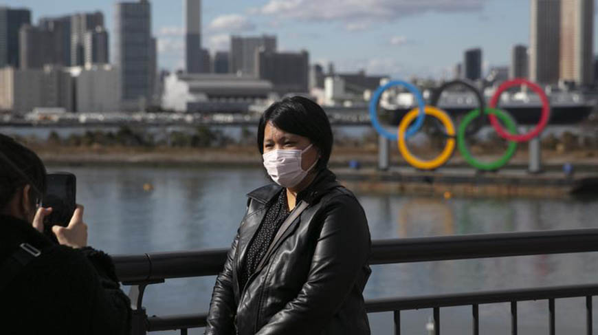 A file photo of a tourist wearing a mask posing for a photo with the Olympic rings in the background, at Tokyo’s Odaiba district (AFP photo)